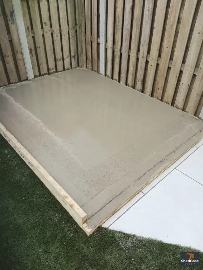 Concrete shed base in a fenced corner beside artificial grass and porcelain paving in Clontarf